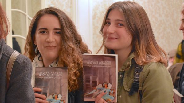 zwei junge Mädchen halten das Neue Testament in modernen Georgisch hoch und freuen sich